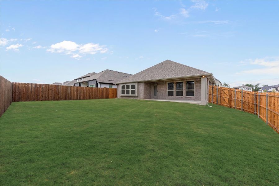 Brick home rear view with large grassy backyard enclosed by wood privacy fence and covered patio Brick home rear view with large grassy backyard enclosed by wood privacy fence and covered patio
