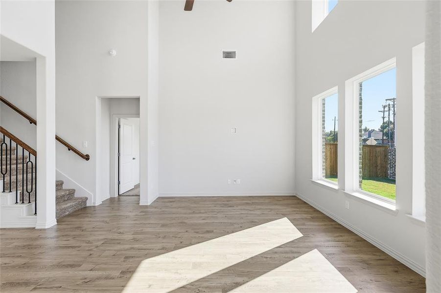 Unfurnished living room featuring healthy amount of natural light, a high ceiling, stairs, light wood-style flooring, and ceiling fan