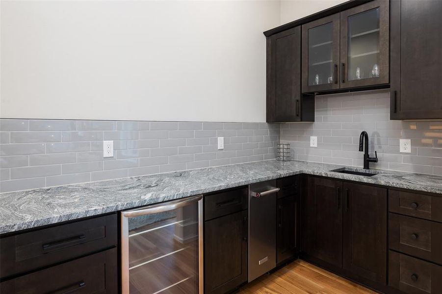 Kitchen featuring light hardwood / wood-style floors, beverage cooler, decorative backsplash, and light stone counters