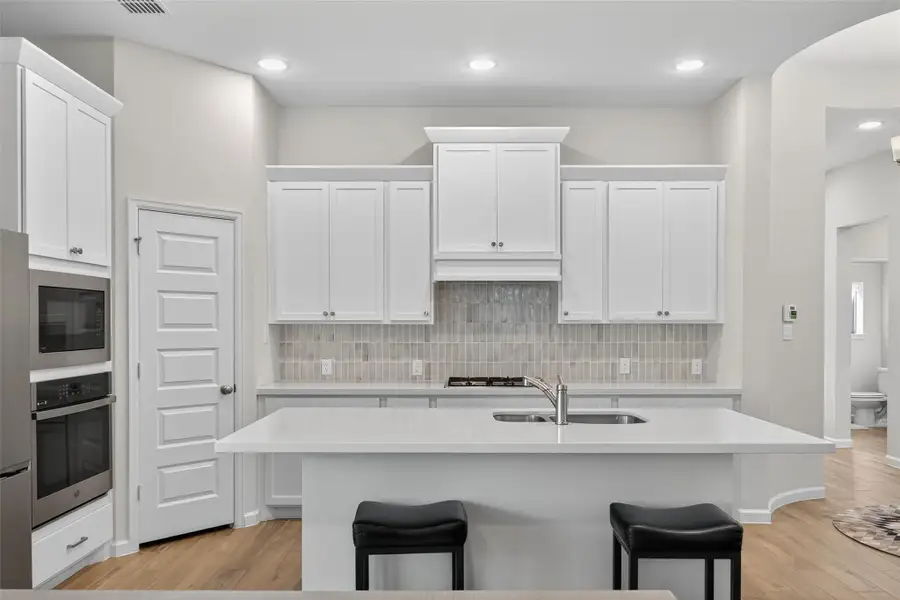 This modern kitchen features white cabinetry, a large island with a sink, stainless steel appliances, quartz countertops, island and a gas cooktop. It opens to a dining area with ample natural light from multiple windows, creating a bright and inviting space. This modern kitchen features white cabinetry, a large island with a sink, stainless steel appliances, quartz countertops, island and a gas cooktop. It opens to a dining area with ample natural light from multiple windows, creating a bright and inviting space.