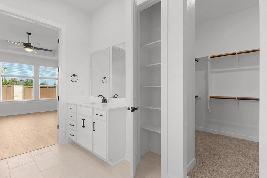 Bathroom featuring a walk in closet, vanity, light tile patterned floors, and light colored carpet