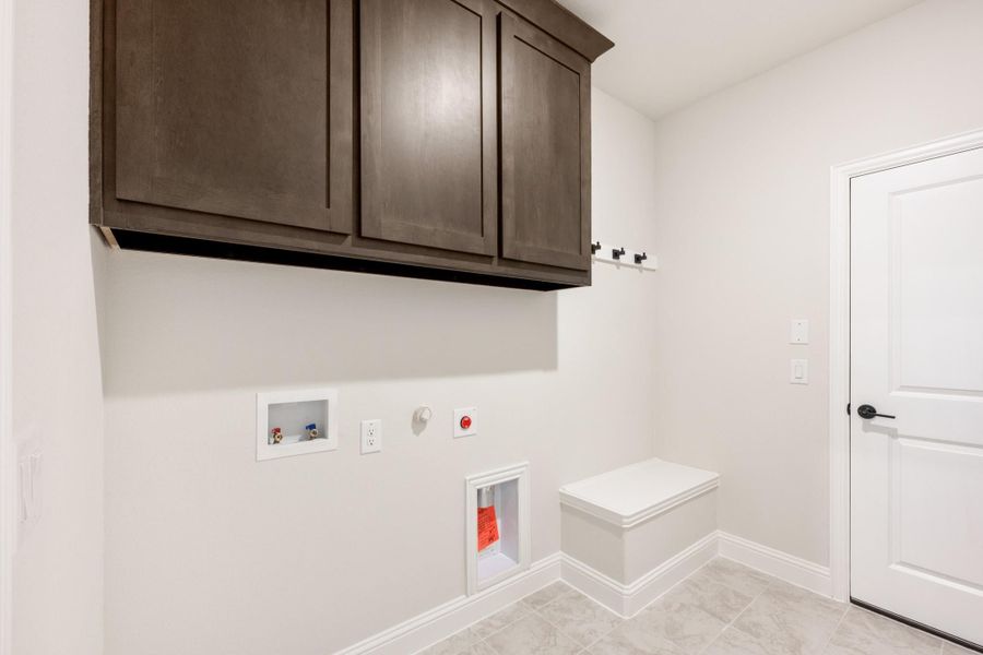 Laundry room with dark wood upper cabinets, washer hookups, wall hooks, and a small built-in bench on tile floors