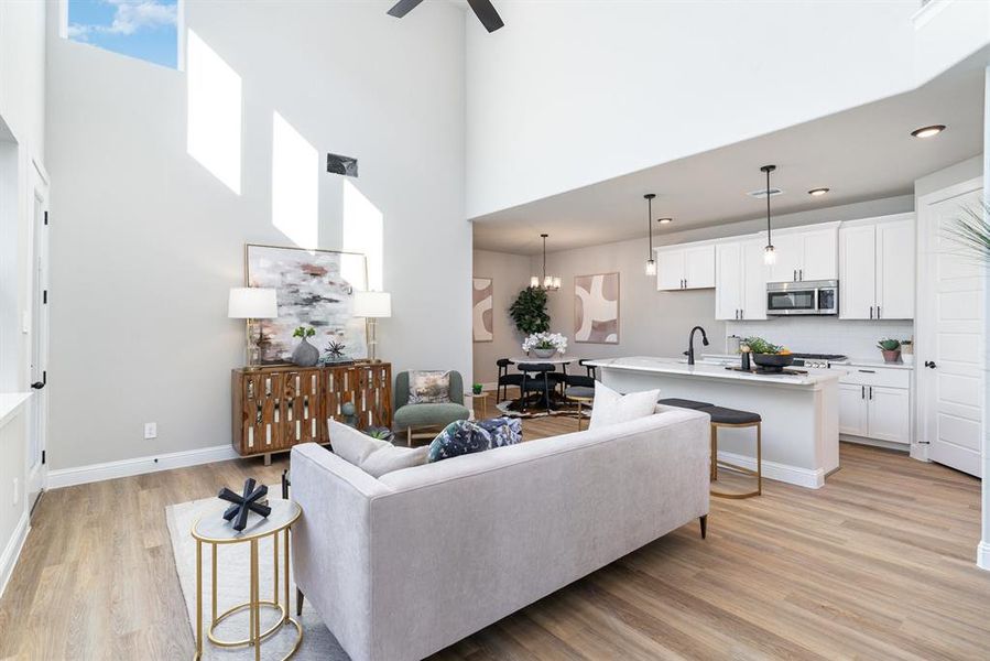 Living room with plenty of natural light, light hardwood / wood-style flooring, ceiling fan with notable chandelier, and a high ceiling