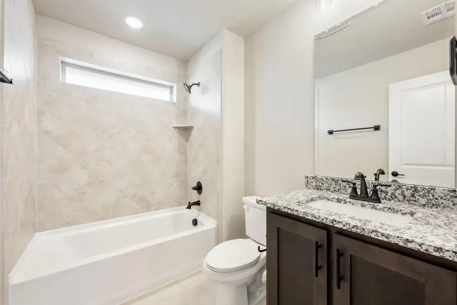 Bathroom with tiled tub-shower combo, dark wood vanity, granite countertop, and black fixtures