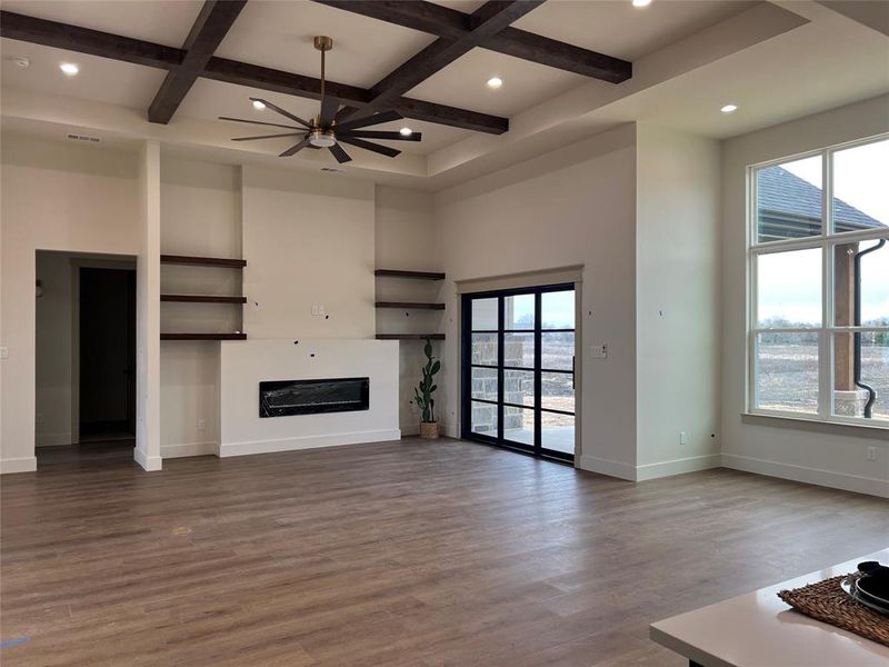 Unfurnished living room with coffered ceiling, a healthy amount of sunlight, hardwood / wood-style floors, and a towering ceiling