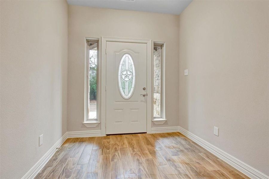 This entryway features a stylish front door with an oval glass insert and star design, flanked by narrow windows. The space is bright with natural light and has warm wood-look flooring, creating a welcoming atmosphere. This entryway features a stylish front door with an oval glass insert and star design, flanked by narrow windows. The space is bright with natural light and has warm wood-look flooring, creating a welcoming atmosphere.