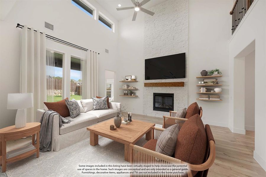 Living room with two-story ceiling, white stone fireplace, ceiling fan, and hardwood floors