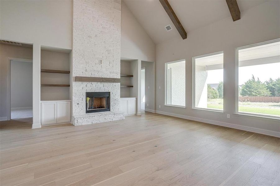 Unfurnished living room featuring light hardwood / wood-style flooring, high vaulted ceiling, beamed ceiling, and built in features