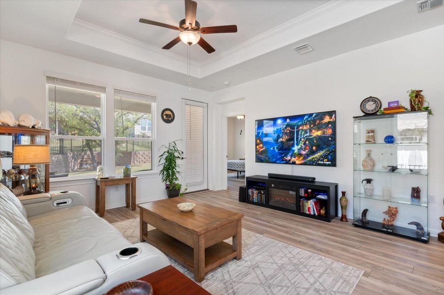 Living area with light wood-style floors, ceiling fan, crown molding, and a raised ceiling Living area with light wood-style floors, ceiling fan, crown molding, and a raised ceiling