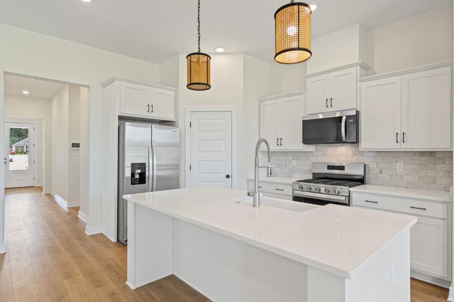 Kitchen featuring a central island with an undermount sink, stainless steel appliances, white cabinetry, wood-finish flooring, and pendant lighting fixtures Kitchen featuring a central island with an undermount sink, stainless steel appliances, white cabinetry, wood-finish flooring, and pendant lighting fixtures