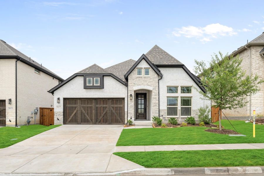 Single-story home with white brick exterior, stone accents, two-car garage with wood doors, and manicured lawn. Single-story home with white brick exterior, stone accents, two-car garage with wood doors, and manicured lawn.