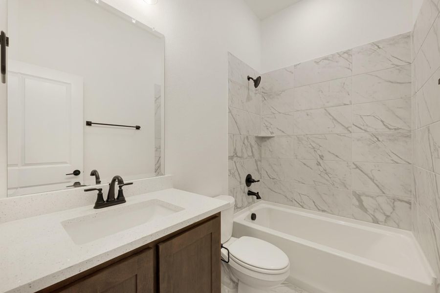Bathroom with marble-tile tub surround, white quartz vanity, dark wood cabinets, and black fixtures