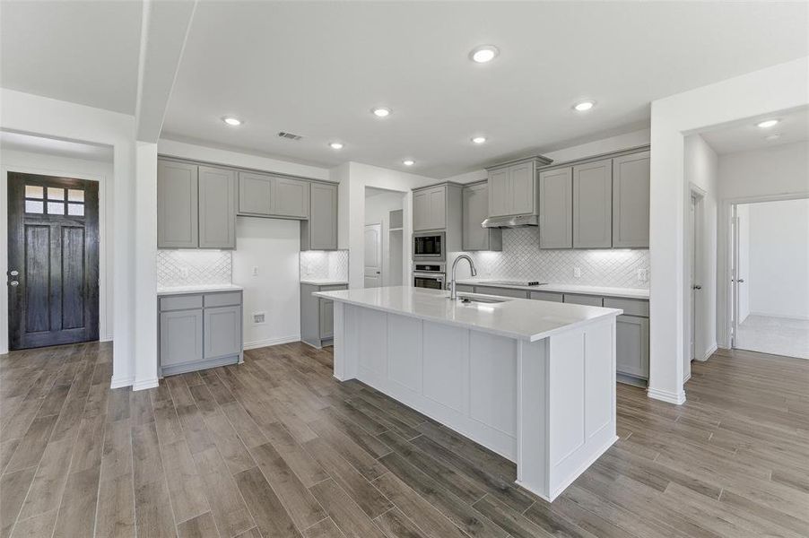Modern kitchen featuring a large central island with a solid surface countertop, light gray cabinetry, and a white subway tile backsplash