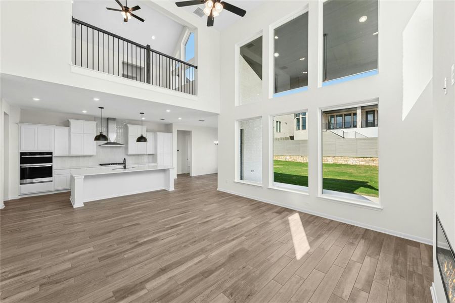 Unfurnished living room with healthy amount of natural light, light wood finished floors, recessed lighting, ceiling fan, and a high ceiling Unfurnished living room with healthy amount of natural light, light wood finished floors, recessed lighting, ceiling fan, and a high ceiling