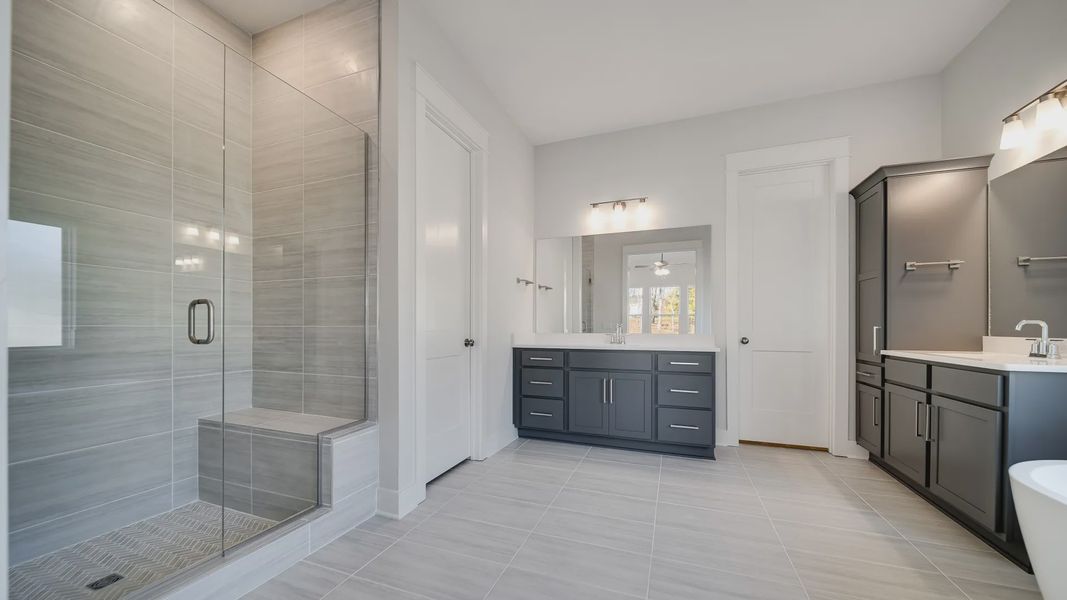 Large tiled bathroom with multiple vanities, glass shower enclosure, and freestanding tub