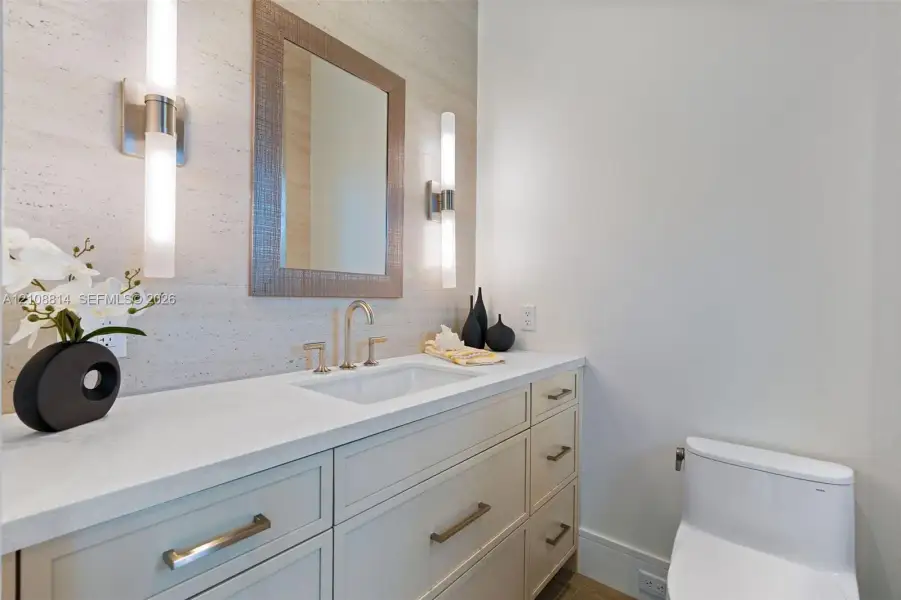 Custom vanity with quartz countertop, undermount sink, stone-finish wall cladding, dual vertical wall-mounted light fixtures, and framed mirror Custom vanity with quartz countertop, undermount sink, stone-finish wall cladding, dual vertical wall-mounted light fixtures, and framed mirror