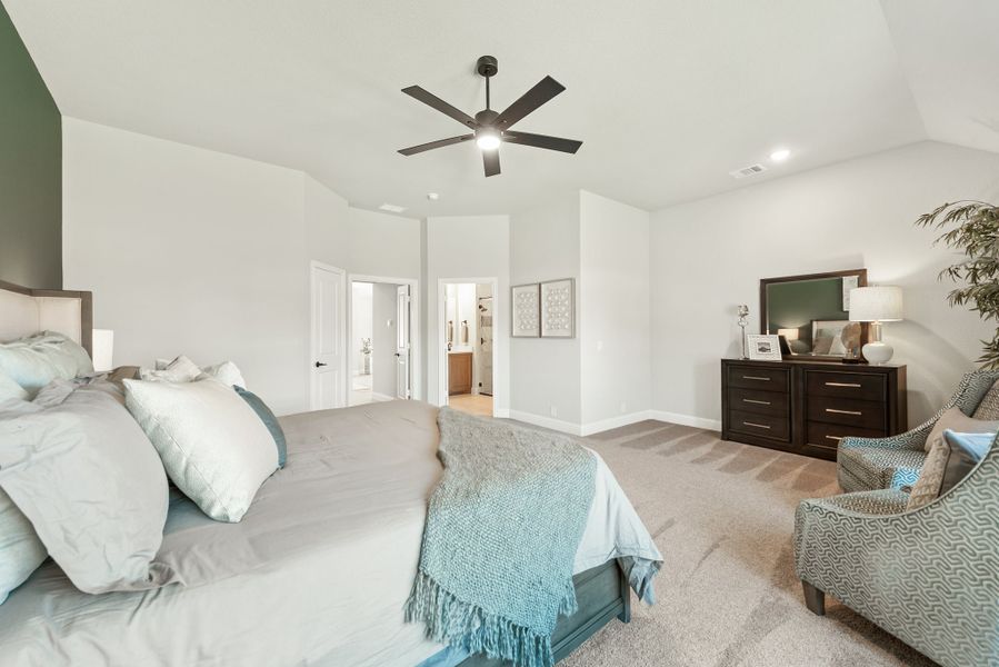 Master bedroom with vaulted ceiling, ceiling fan, dark wood dresser, and open ensuite bathroom door