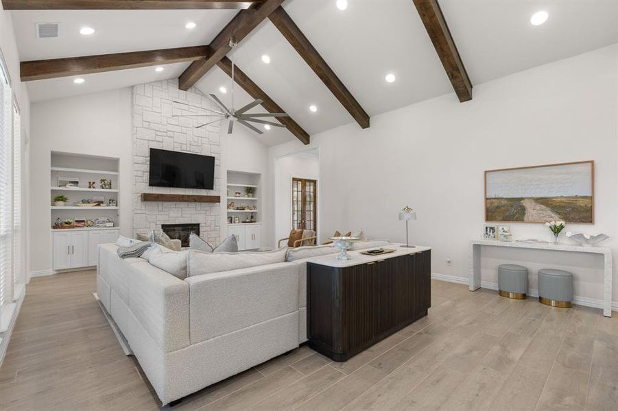 Living room featuring a stone fireplace, light wood-type flooring, ceiling fan, high vaulted ceiling, and beamed ceiling Living room featuring a stone fireplace, light wood-type flooring, ceiling fan, high vaulted ceiling, and beamed ceiling