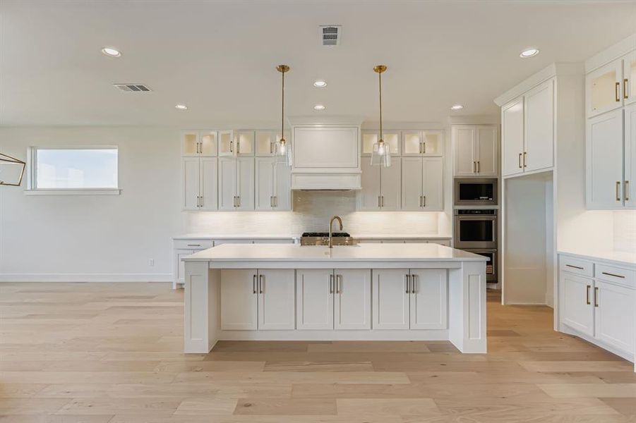 Kitchen with glass insert cabinets, white cabinetry, a kitchen island with sink, recessed lighting, and hanging light fixtures
