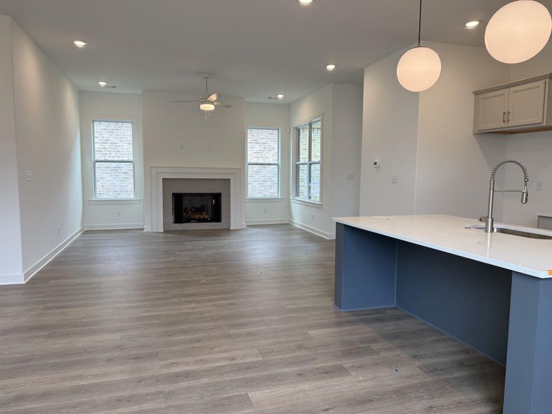 Open-concept living area featuring a fireplace with a white mantel, recessed lighting, wood-finish flooring, and a kitchen island with a white countertop