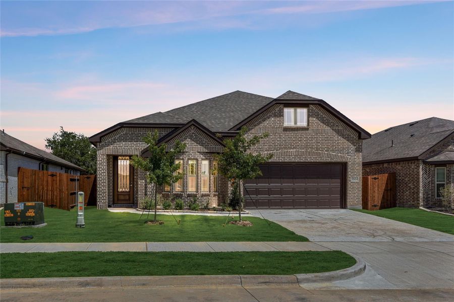 Single-story brick home with dark two-car garage, arched entry, and manicured front lawn at dusk