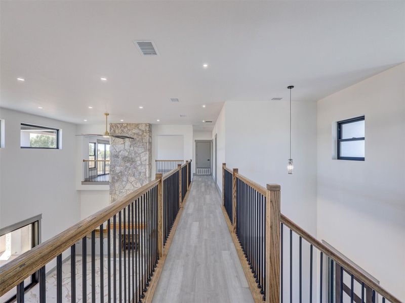 An upper-level walkway with wooden handrails overlooks the light-filled lower living areas.