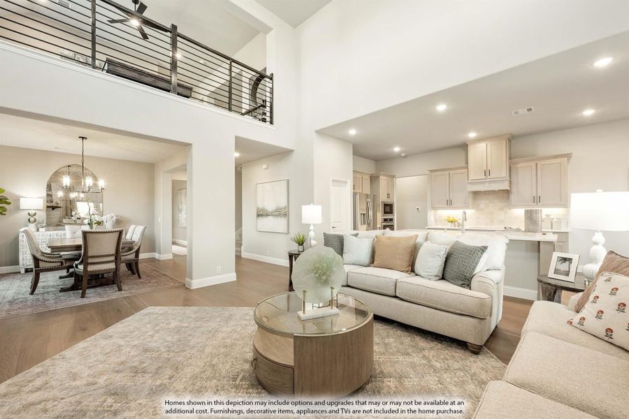 Open-concept living room with two-story ceiling, upper balcony, and views into dining area and kitchen