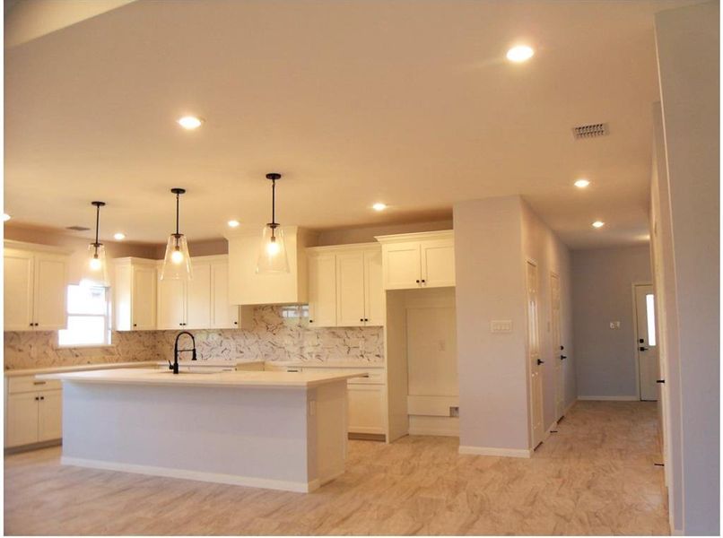 Kitchen featuring sink, an island with sink, backsplash, white cabinetry, and pendant lighting