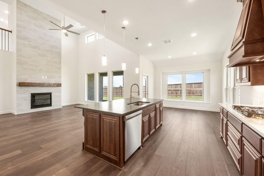 Open kitchen with dark wood island, hardwood floors, and fireplace in adjacent living area with high ceilings Open kitchen with dark wood island, hardwood floors, and fireplace in adjacent living area with high ceilings