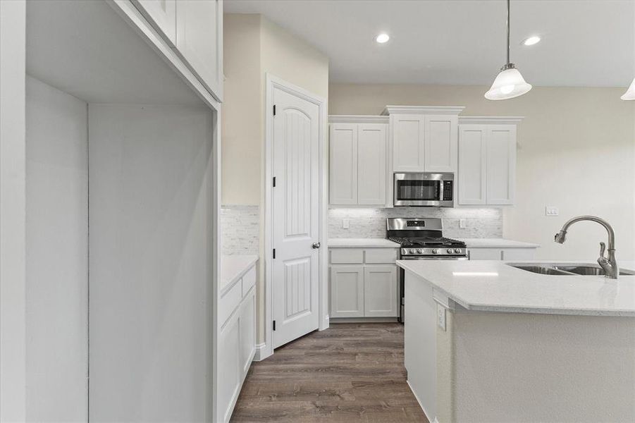 Kitchen with appliances with stainless steel finishes, backsplash, white cabinetry, dark wood-style flooring, and hanging light fixtures