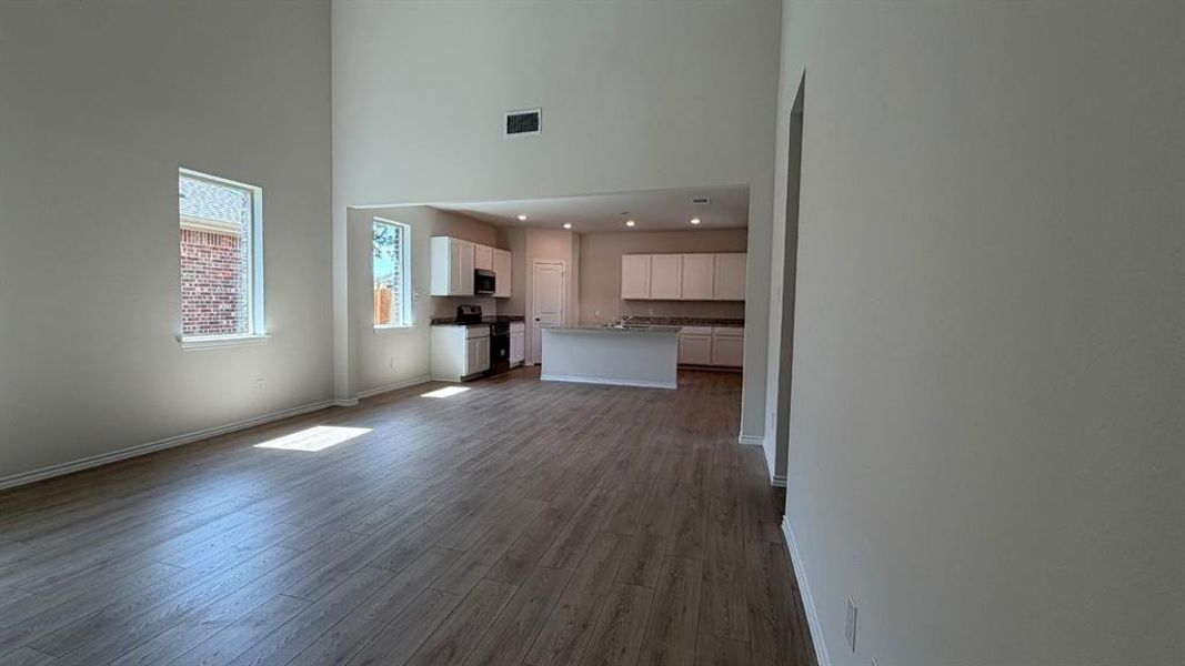 Spacious living area featuring high ceilings, wood-finish flooring, and multiple windows Spacious living area featuring high ceilings, wood-finish flooring, and multiple windows