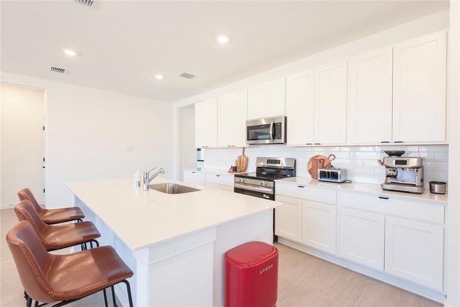 Kitchen featuring white cabinets, light wood-type flooring, stainless steel appliances, a center island with sink, and recessed lighting Kitchen featuring white cabinets, light wood-type flooring, stainless steel appliances, a center island with sink, and recessed lighting
