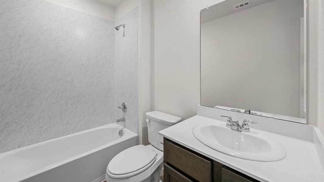 Full bathroom featuring a white tub with shower, white toilet, and a vanity with an integrated sink and chrome fixtures