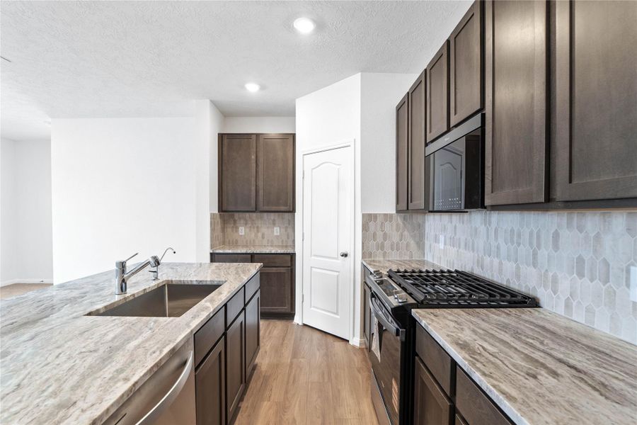A true chef’s dream, this expansive kitchen boasts high ceilings, rich stained wood cabinets, granite countertops, stainless steel appliances, a modern tile backsplash, recessed lighting, extended counter space, an island with a single bowl sink, and a walk-in pantry—all with a clear view of the spacious Great Room.