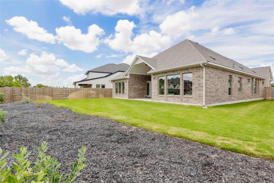 A neatly manicured lawn borders the modern brick exterior of this inviting home, framed by a wooden fence and clear skies.