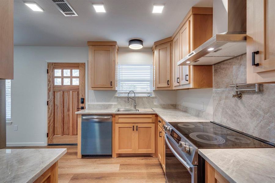 Kitchen featuring appliances with stainless steel finishes, wall chimney exhaust hood, sink, and light brown cabinets