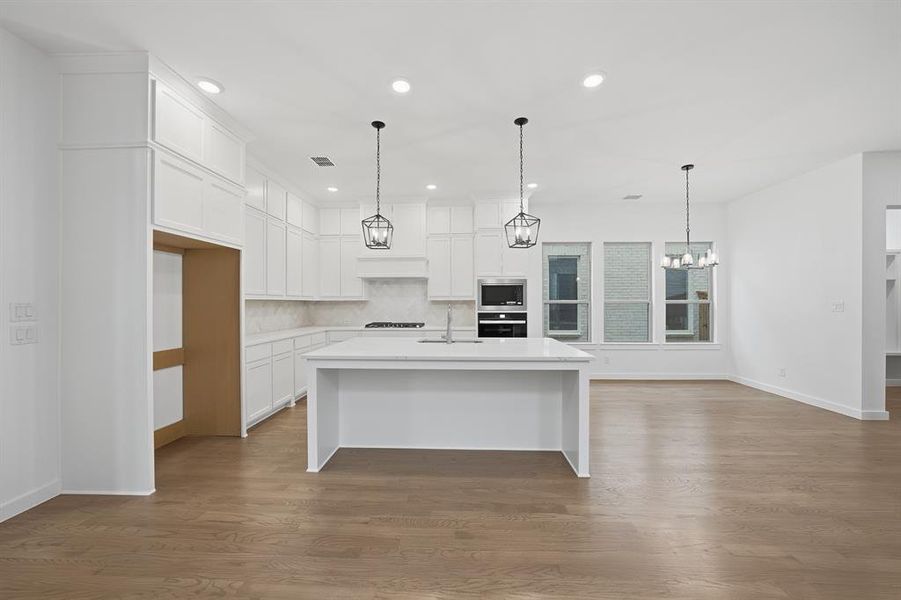 Kitchen with a breakfast bar area, white cabinets, decorative light fixtures, an island with sink, and light stone counters