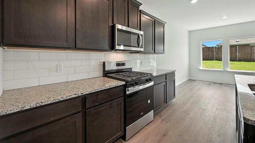Kitchen with stainless steel appliances, dark wood finish cabinetry, light wood-style floors, light stone counters, and backsplash