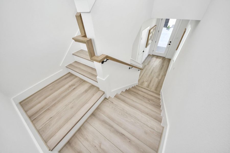 Bright, modern staircase with sleek wood flooring and white walls, leading to an inviting entryway with natural light.