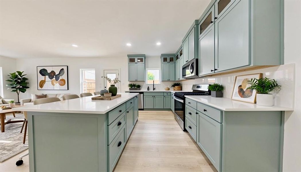 Spacious kitchen featuring light green cabinetry, a central island with a white countertop, and stainless steel appliances