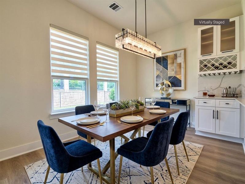 Dining area featuring a linear chandelier, wood-finish flooring, two large windows with blinds, and an integrated wet bar with white cabinetry and a wine rack