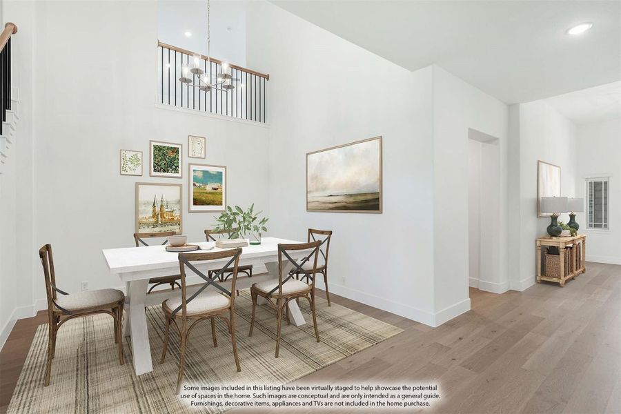Dining room with two-story ceiling, white table, wood chairs, chandelier, and hardwood floors