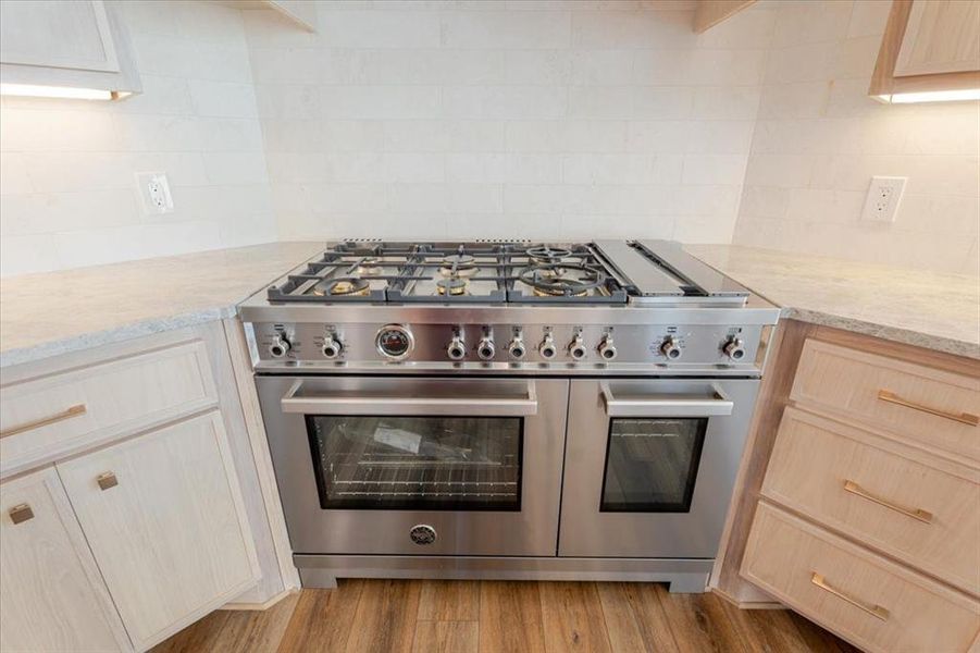 Kitchen with decorative backsplash, light wood finished floors, light brown cabinets, and range with two ovens Kitchen with decorative backsplash, light wood finished floors, light brown cabinets, and range with two ovens