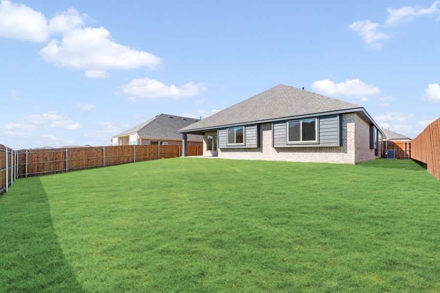 Backyard of single-story brick home with large green lawn, covered patio, and wood privacy fence