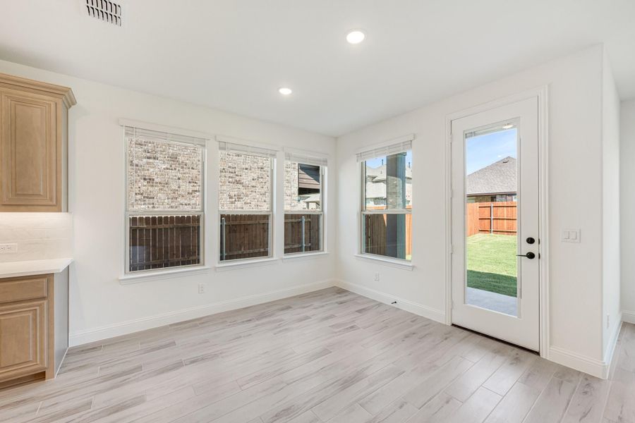 Bright dining area with light wood-look floors, three windows, and a glass back door leading to a fenced yard. Bright dining area with light wood-look floors, three windows, and a glass back door leading to a fenced yard.
