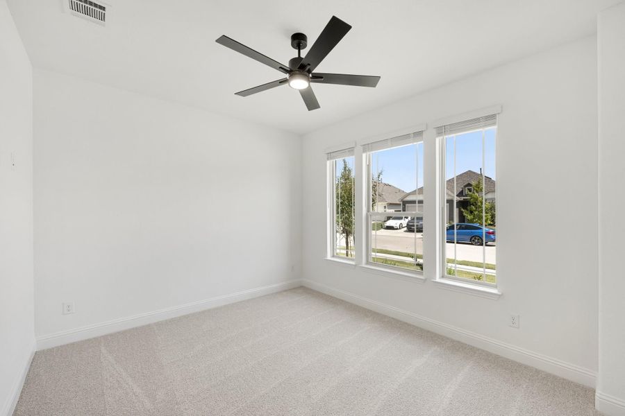 Empty bedroom with white walls, carpet flooring, ceiling fan, and triple windows overlooking a neighborhood street. Empty bedroom with white walls, carpet flooring, ceiling fan, and triple windows overlooking a neighborhood street.