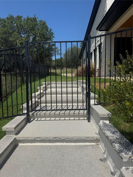 Secure iron fencing leads to stone steps accessing this charming residence with clear blue skies above.