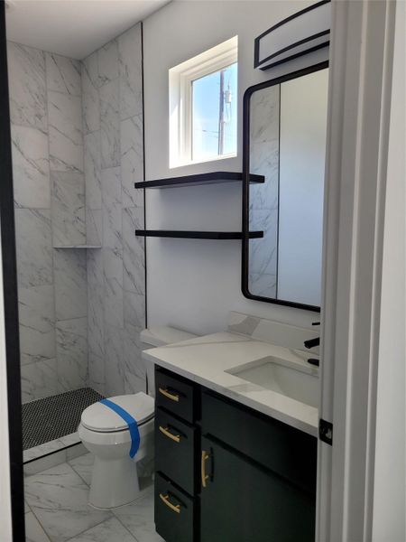 Bathroom featuring vanity, a marble finish shower, and light marble finish flooring