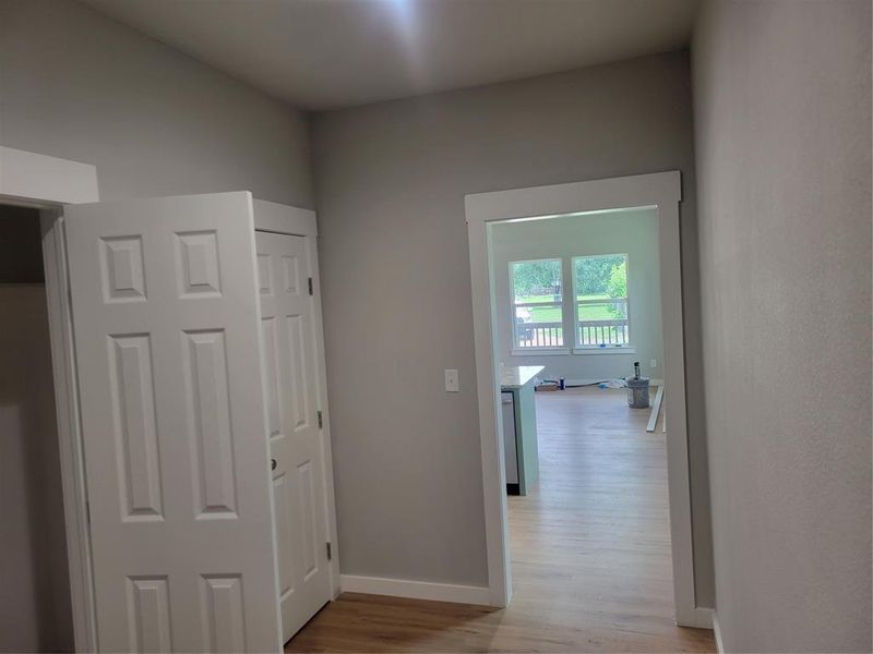 Interior hallway featuring a light gray wall color, white trim, and wood-finish flooring