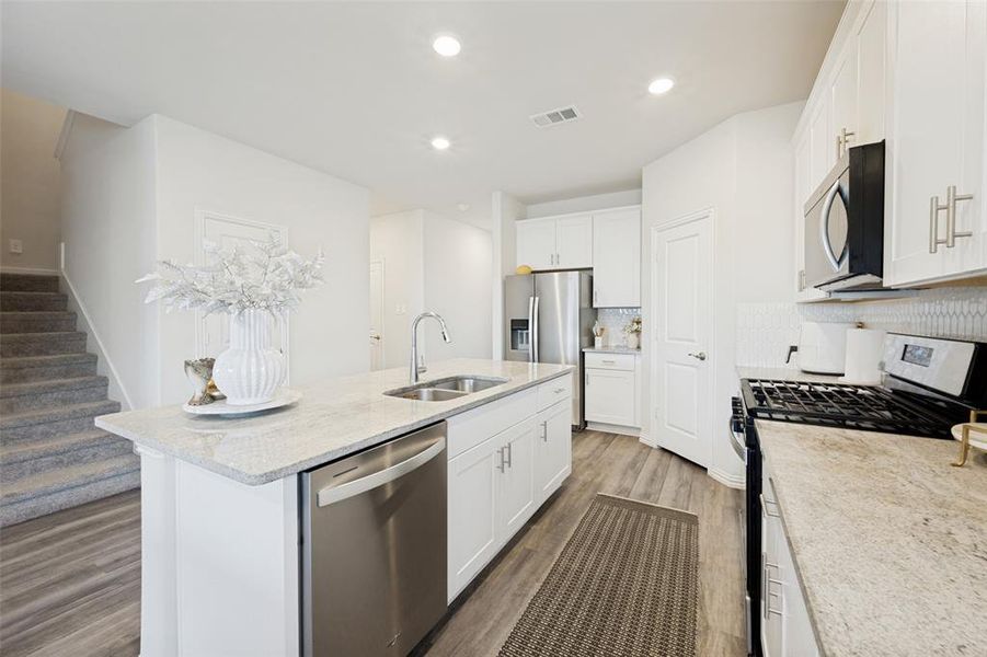 Modern kitchen featuring an island with a double basin sink, stainless steel dishwasher, and light-toned countertop Modern kitchen featuring an island with a double basin sink, stainless steel dishwasher, and light-toned countertop